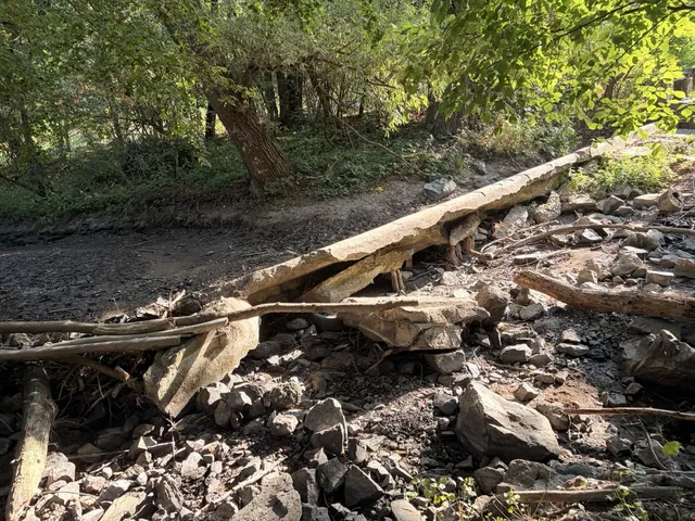 Poškozená betonová deska vodní stavby nakloněná přes kamenité dno vyschlého koryta